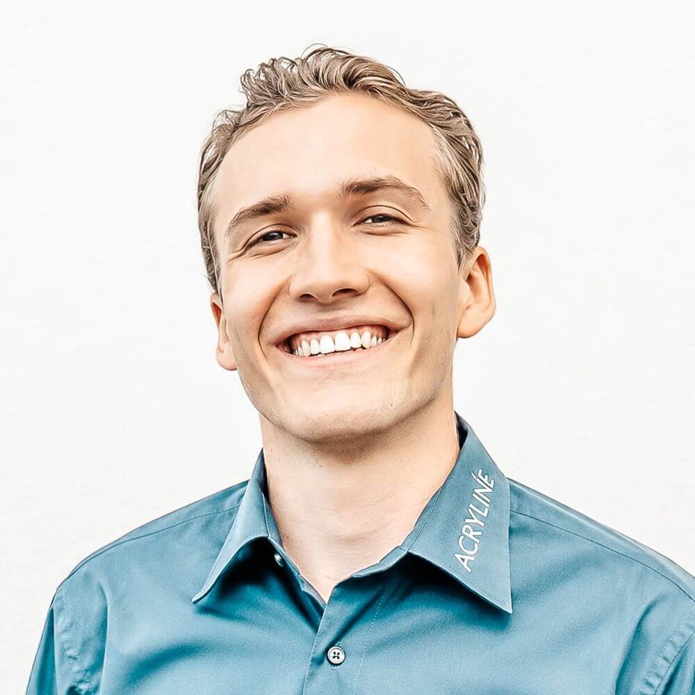 Pius Laim Young man with short blond hair smiling broadly, wearing a teal button-up shirt against a light background.